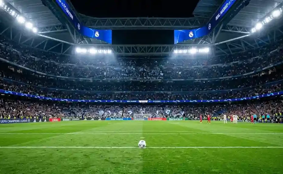 Wide-angle night shot of Santiago Bernabéu Stadium lit up under floodlights with a football on the center circle during a Champions League match.